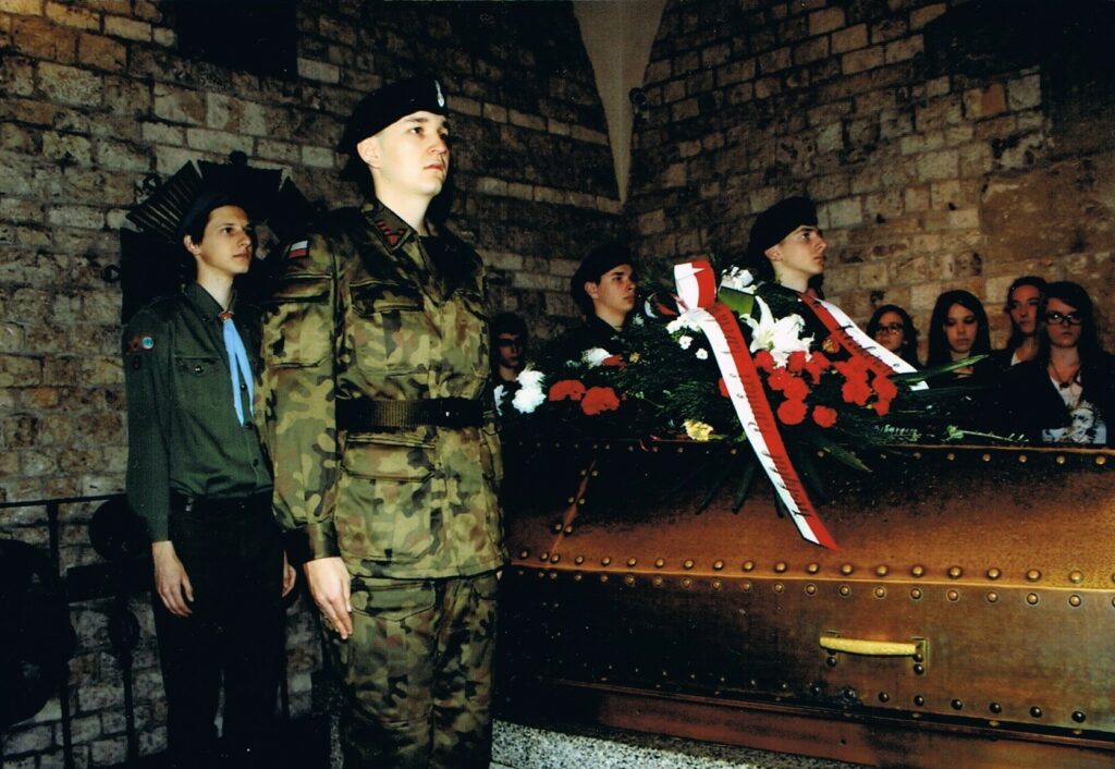 Młody Maciej Wcisło w mundurze instruktora ZHP pełni wartę honorową przy trumnie Marszałka Józefa Piłsudskiego w Krypcie pod Wieżą Srebrnych Dzwonów na Wawelu. Obok widoczny harcerz Krzysztof Rollauer oraz warta Związku Strzeleckiego. Uroczystość 80. rocznicy śmierci Marszałka.