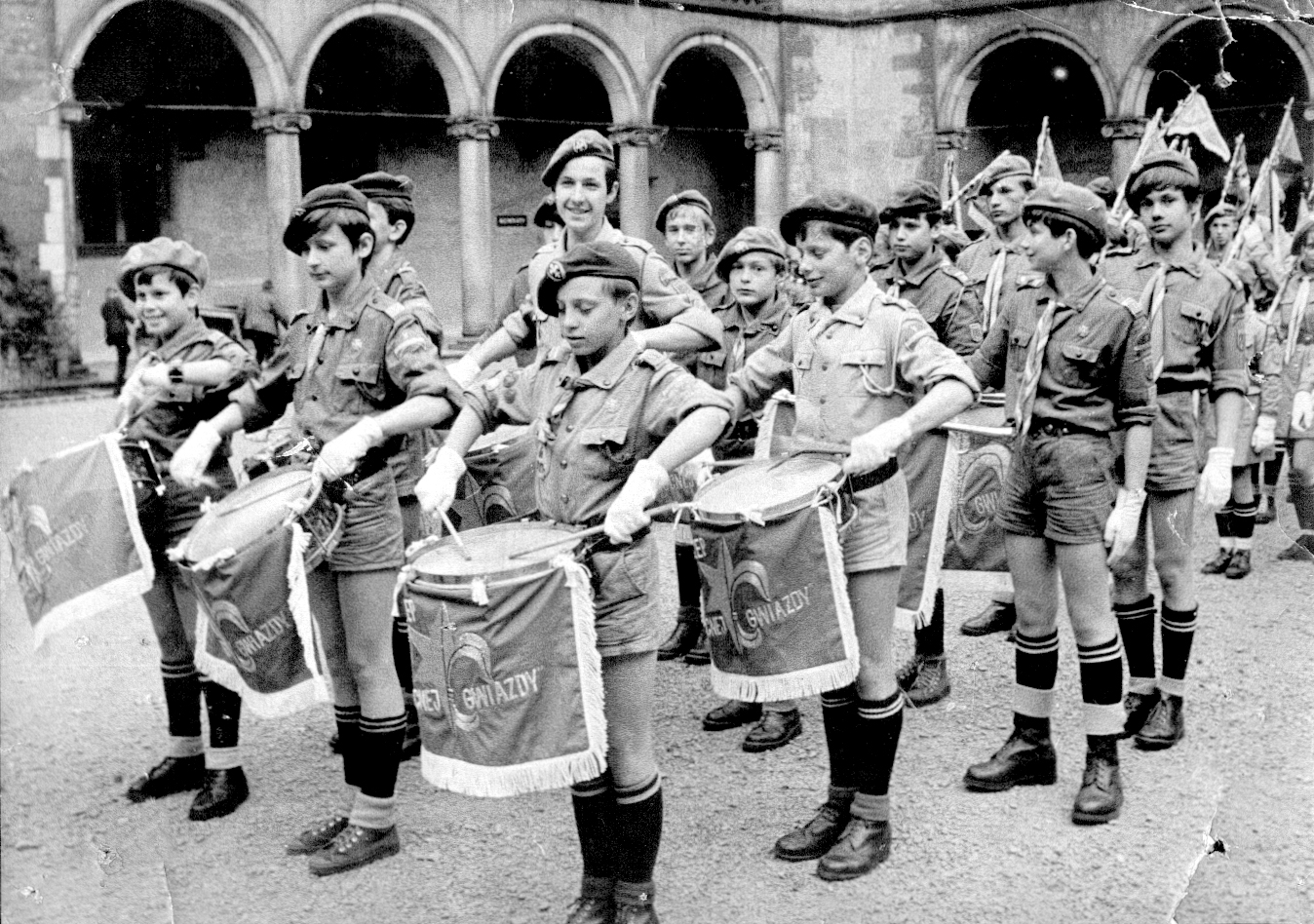 Archiwalna fotografia z dziedzińca Zamku Królewskiego na Wawelu (23 maja 1970). Uroczystość nadania Szczepowi „Północna Gwiazda” imienia gen. Mariusza Zaruskiego oraz wręczenia sztandaru. Widoczny poczet werblistów i fanfarzystów z historycznymi proporcami (płomieniami do fanfar) haftowanymi w Spółdzielni im. St. Wyspiańskiego.