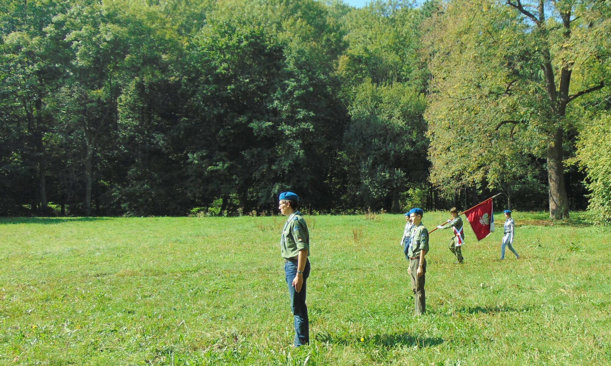 Uroczysty apel harcerski na zielonych błoniach pod zamkiem w Korzkwi. Na pierwszym planie dh Andrzej Batkiewicz prowadzący apel, w centrum poczet wprowadzający czerwony sztandar szczepu z wyhaftowanym orłem. W centrum Maciej Wcisło w mundurze instruktorskim jako pomysłodawca komendant zlotu 50-lecia Szczepu ZHP „Północna Gwiazda”. Podniosła atmosfera, wrzesień 2015.